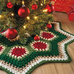 Puede incluir: Una falda de árbol de Navidad de crochet verde, roja y blanca con un diseño de estrella. La falda se coloca debajo de un árbol de Navidad decorado con adornos rojos y luces blancas.