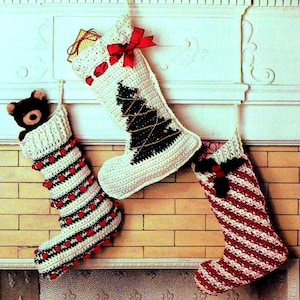 May include: Three handmade Christmas stockings hang from a fireplace mantel. One is white with a black Christmas tree design, another is red and white striped, and the third is white with red pom-poms and a teddy bear inside. A red bow adorns the top of one stocking.