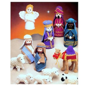 May include: A crocheted nativity scene with a white angel, three wise men, a camel, a shepherd, and sheep. The wise men are wearing purple, red, and blue robes. The camel is brown and has a purple saddle. The shepherd is wearing a blue robe and has a brown beard. The sheep are white and have black eyes.