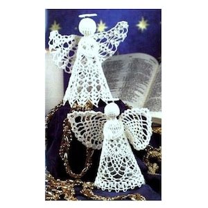 May include: Two white crocheted angels, one larger than the other, with delicate lace details. The angels are sitting on a purple surface with gold chains.