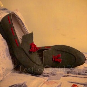 May include: A pair of dark green suede loafers with red tassel accents. The loafers have a pointed toe and a low heel.