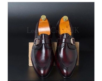 Può includere: Un paio di scarpe in pelle bordeaux con un cinturino con fibbia singola. Le scarpe hanno una punta a punta e un design a punta alare.