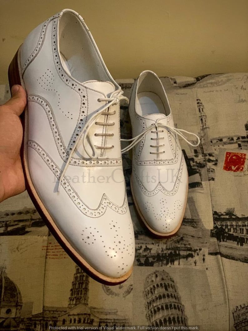 Puede incluir: Un par de zapatos de vestir de cuero blanco con dise&ntilde;o de punta de ala y cierre de cordones. Los zapatos tienen una suela de cuero marr&oacute;n y una parte superior de cuero blanco.