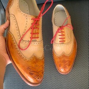 May include: Two pairs of brown leather brogue shoes with red laces. The shoes have a wingtip design and are made of distressed leather.