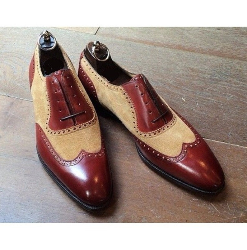 May include: A pair of brown and tan leather shoes with wingtip detailing. The shoes have a lace-up closure and a pointed toe.