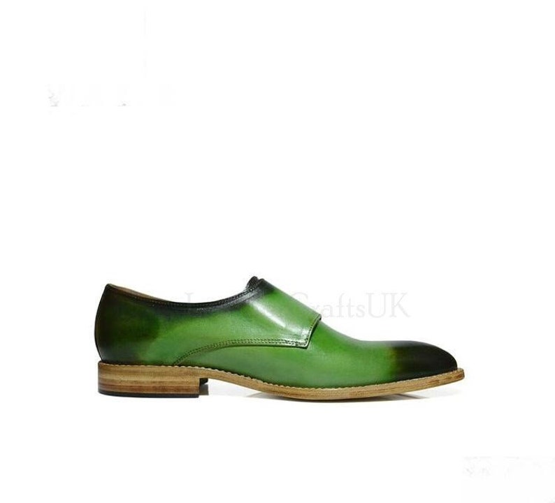 May include: Green leather dress shoes with a single buckle strap. The shoes have a brown leather sole.