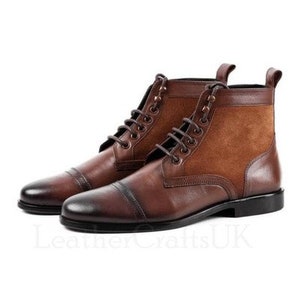 May include: Brown leather boots with a suede panel on the back. The boots have a lace-up closure and a cap toe.