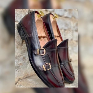 May include: A pair of burgundy leather loafers with gold buckles. The loafers have a pointed toe and a slip-on design.
