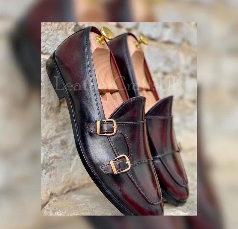 May include: A pair of burgundy leather loafers with gold buckles. The loafers have a pointed toe and a slip-on design.