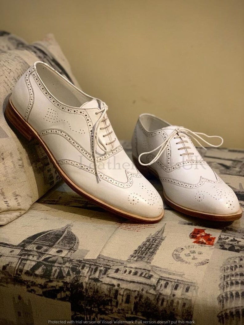 Puede incluir: Un par de zapatos de vestir de cuero blanco con cordones. Los zapatos tienen un dise&ntilde;o perforado y una suela de cuero marr&oacute;n.