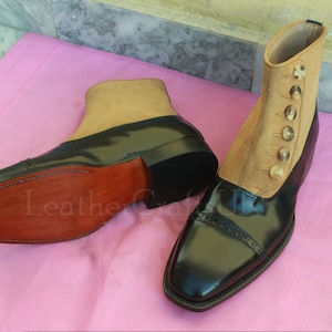 Puede incluir: Un par de botines de cuero negro con parte superior de ante marrón. Las botas tienen cierre de botón y punta puntiaguda.