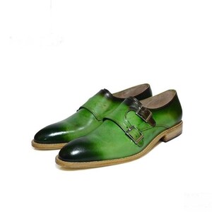 May include: A pair of green leather dress shoes with double monk straps. The shoes have a brown leather sole and a pointed toe.