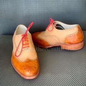 May include: Two pairs of brown leather Oxford shoes with wingtip detailing. The shoes have a tan leather upper and a brown leather sole. The laces are a bright pink colour.