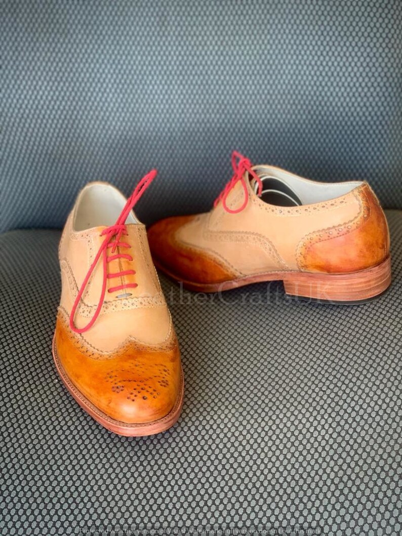 May include: Two pairs of brown leather Oxford shoes with wingtip detailing. The shoes have a tan leather upper and a brown leather sole. The laces are a bright pink colour.