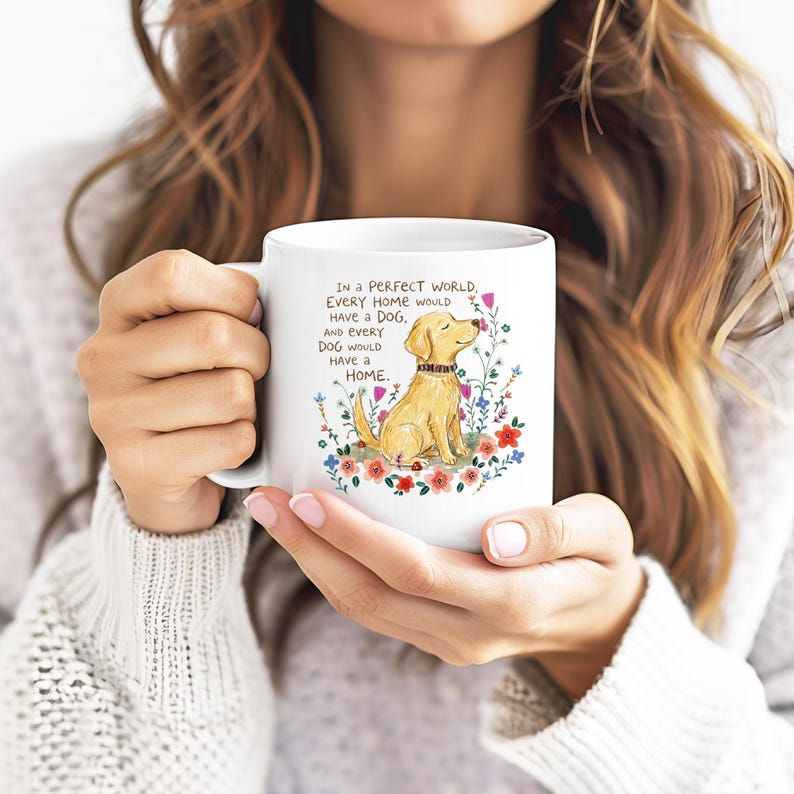 May include: A white ceramic mug featuring a colorful illustration of a golden dog sitting amidst various wildflowers. The text printed on the mug reads: In a perfect world, every home would have a dog, and every dog would have a home.