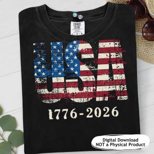 Pode incluir: Camiseta preta com um design desgastado da bandeira dos EUA em vermelho, branco e azul. A palavra "USA" é exibida em destaque, com os anos "1776-2026" abaixo. A camisa é da marca Comfort Colors.