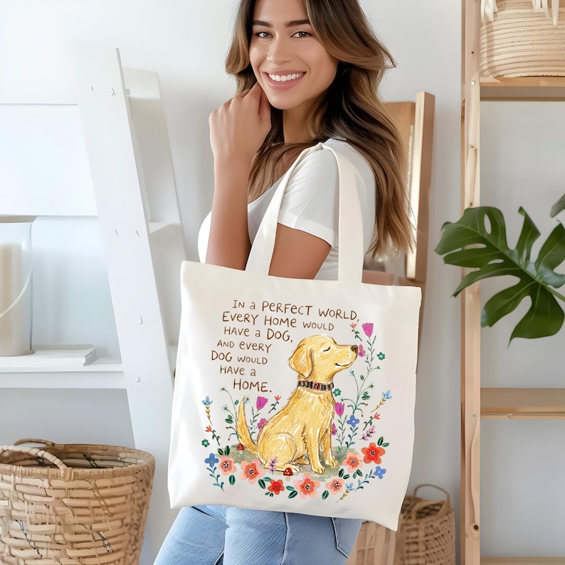 May include: A white canvas tote bag featuring a golden retriever illustration surrounded by colorful flowers. The text reads: In a PERFECT WORLD, EVERY HOME WOULD HAVE A DOG, AND EVERY DOG WOULD HAVE A HOME. The design is centered on the front panel.