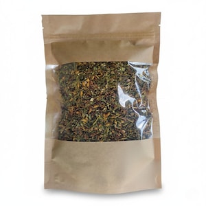 May include: A brown paper bag with a transparent panel, containing a mixture of dried herbs and spices. The contents are a blend of green, brown, and yellow, indicating a variety of culinary ingredients. The bag is sealed at the top.