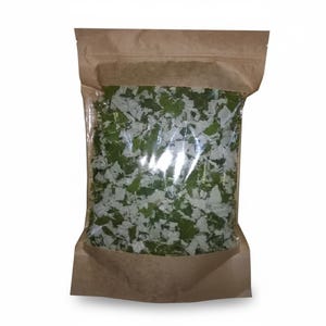 May include: A clear plastic bag filled with dried green herbs, sealed inside a brown paper bag. The herbs appear to be leafy and have a light green and white colour. The bag is sealed at the top.
