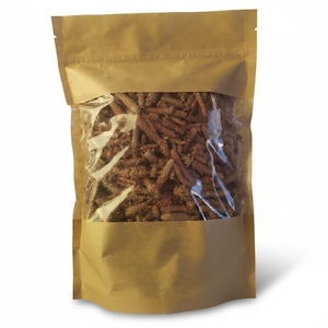 May include: A brown paper bag with a clear window, filled with dried, brown plant material. The bag is sealed at the top and has a visible zip closure. The contents appear to be a natural product.