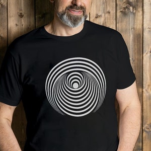 May include: A man wearing a black t-shirt with a white and black optical illusion graphic. The graphic is a circle with concentric rings.