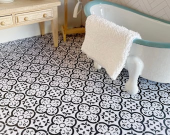 May include: A dollhouse bathroom with a white porcelain bathtub with a blue rim, a white towel hanging over the side, and a black and white patterned tile floor.