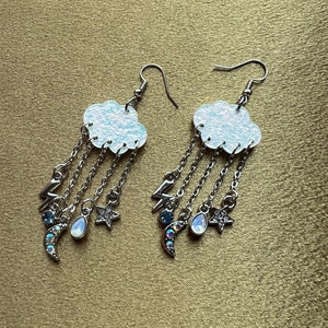 Puede incluir: Un par de pendientes colgantes de plata con un dije de nube blanca y dijes colgantes de lunas, estrellas y rayos.