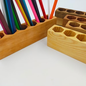 May include: Two wooden pencil holders, one with six compartments and the other with five compartments. The holder with six compartments is made of light wood and the holder with five compartments is made of darker wood. Both holders are empty.