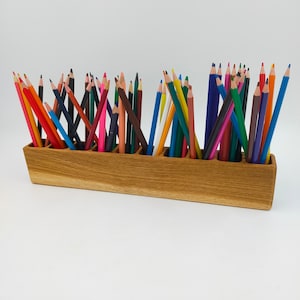Puede incluir: Un porta lápices de madera con ocho compartimentos, lleno de lápices de colores variados. Los lápices están dispuestos en un patrón aleatorio, con algunos sobresaliendo del porta lápices.
