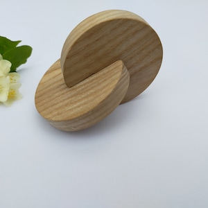 May include: A wooden toy made of two interlocking half-circles. The toy is made of light brown wood and has a smooth, polished finish.