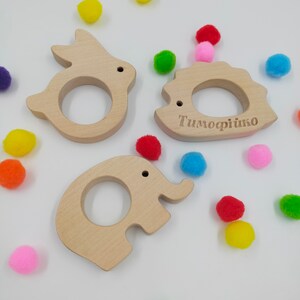 May include: Three wooden teethers shaped like a rabbit, hedgehog, and elephant. The hedgehog teether is engraved with the name "Timofeyko".
