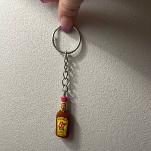 May include: Miniature Heinz 57 sauce bottle keychain. The brown bottle has a yellow label with red text and a pink cap. The keychain is attached to a silver chain and ring.