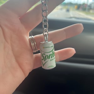 May include: A silver keychain with a miniature Sprite can charm. The can is white with green lettering and says "Sprite Zero Sugar Lemon Lime".