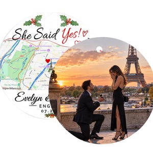 May include: A circular ornament featuring a map of Paris with a red heart marker, the text She Said Yes!, and a photograph of a marriage proposal in front of the Eiffel Tower at sunset. The design includes holly accents and space for names and dates.