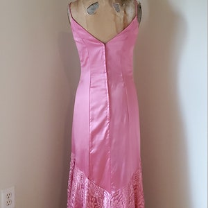May include: A pink satin and lace formal gown with a V-neckline and a fitted bodice. The skirt is a mermaid style with a lace overlay.