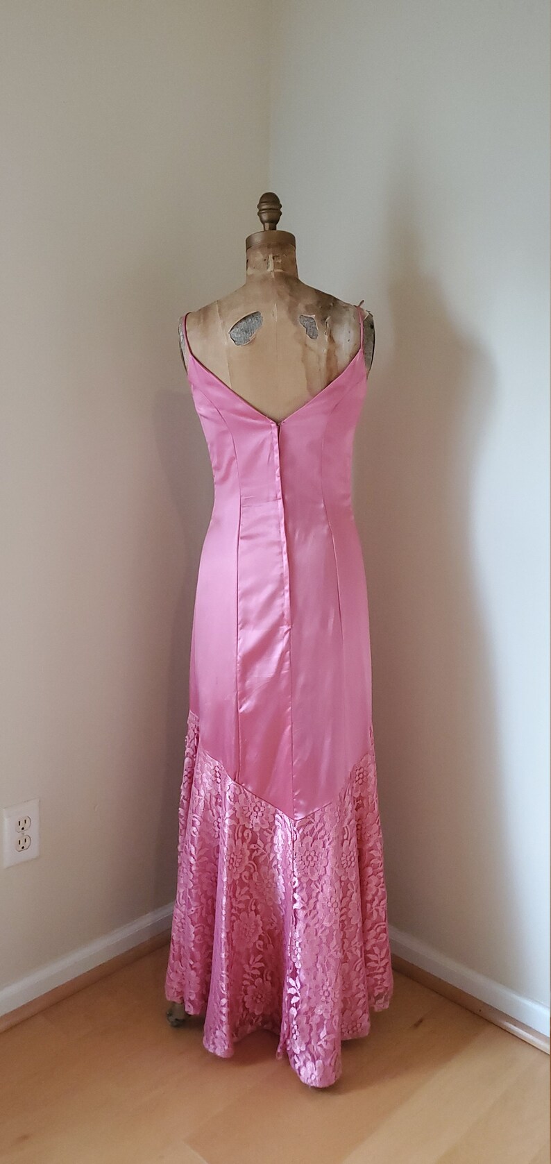 May include: A pink satin and lace formal gown with a V-neckline and a fitted bodice. The skirt is a mermaid style with a lace overlay.
