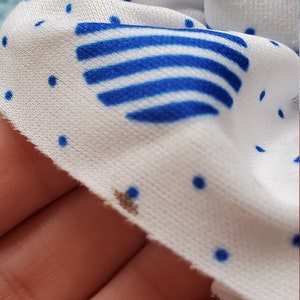 May include: White fabric with blue polka dots and a blue and white striped design. There is a small brown stain on the fabric.