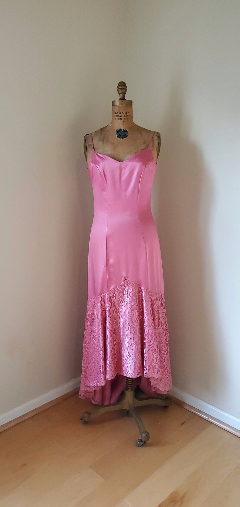 May include: A pink satin dress with a lace hem. The dress is on a dress form and has a sweetheart neckline.