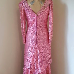May include: A pink lace dress with long sleeves and a V-neckline. The dress has a tiered skirt and a lace-up back.