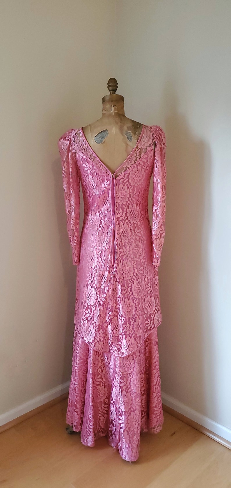 May include: A pink lace dress with long sleeves and a V-neckline. The dress has a tiered skirt and a lace-up back.
