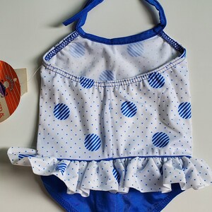 May include: A blue and white polka dot swimsuit with a ruffled bottom and a halter top. The swimsuit has a blue trim and a white background with blue polka dots.
