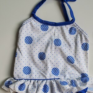 May include: A white and blue polka dot swimsuit with a blue ruffle trim and a blue halter strap.