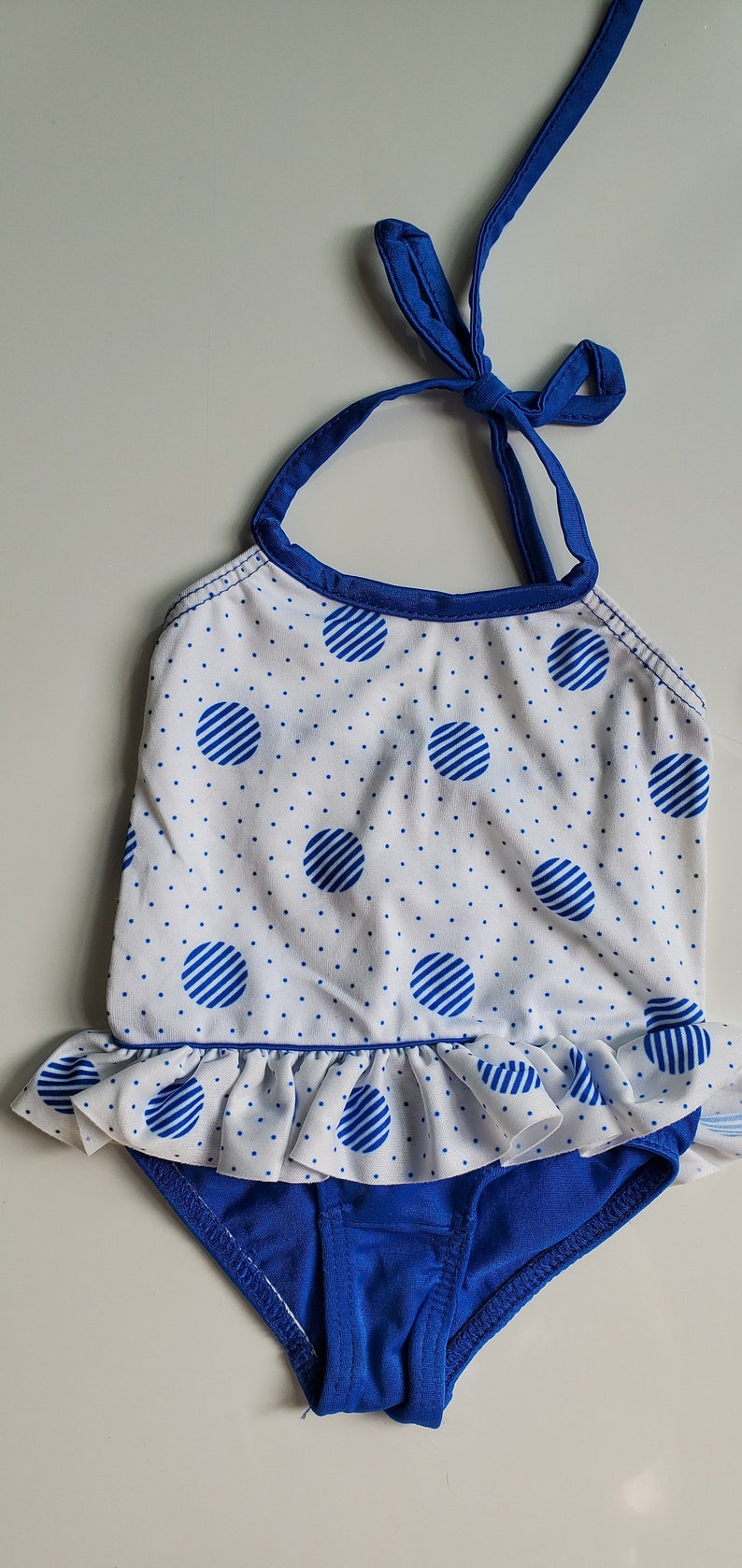 May include: A white and blue polka dot swimsuit with a blue ruffle trim and a blue halter strap.