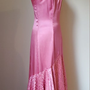 May include: A pink satin and lace dress with a high-low hemline. The dress has a fitted bodice and a flowing skirt.