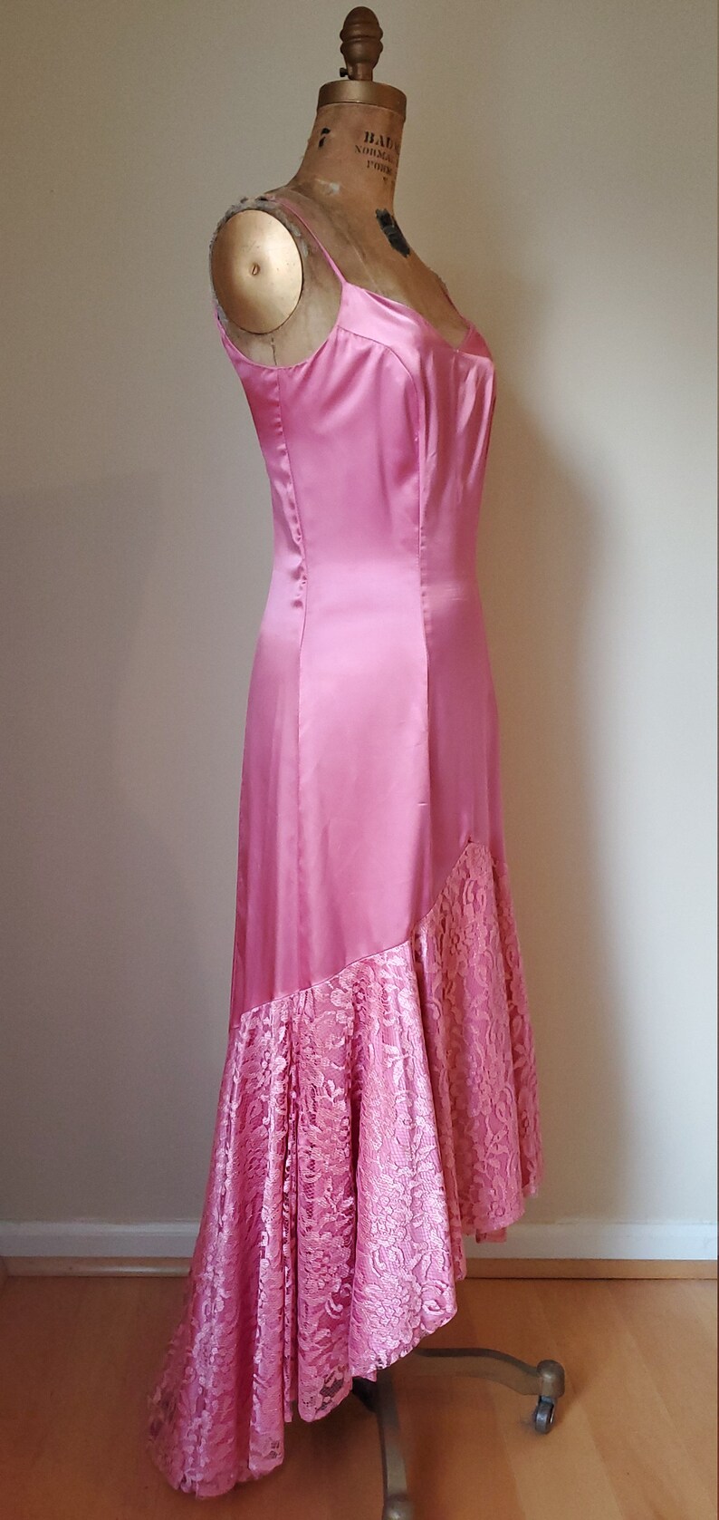 May include: A pink satin and lace dress with a high-low hemline. The dress has a fitted bodice and a flowing skirt.