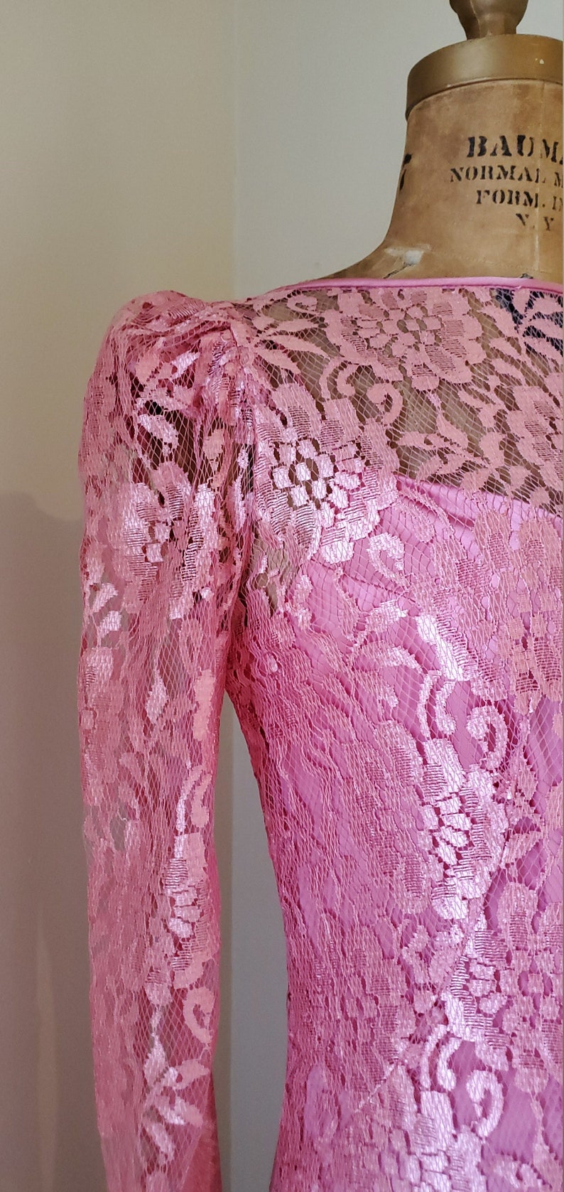 May include: A pink lace dress with long sleeves and a round neckline. The dress is made of delicate lace with a floral pattern.