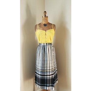 May include: A black and white plaid wrap skirt with a yellow and blue stripe detail. The skirt is made of a thick, woven fabric and has a fringed hem.