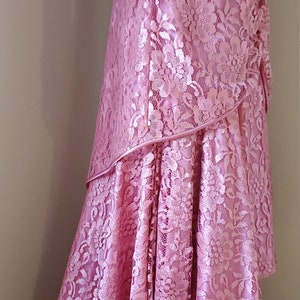 May include: A long, pink lace dress with a high neckline and long sleeves. The dress has a layered skirt with a ruffled hem.