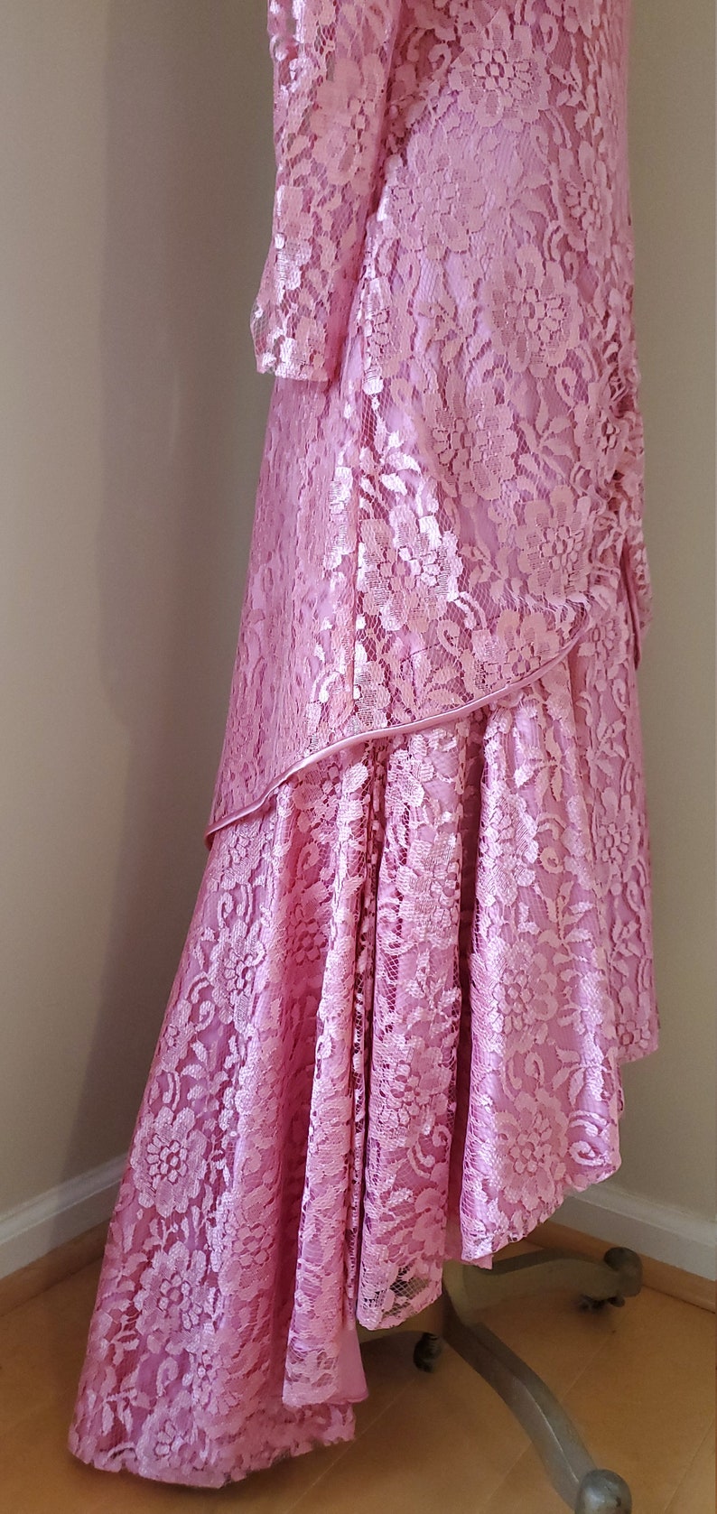 May include: A long, pink lace dress with a high neckline and long sleeves. The dress has a layered skirt with a ruffled hem.