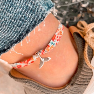 Peut inclure: Un bracelet de cheville en tissu floral coloré avec un charme de queue de baleine argenté.